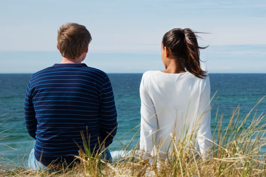 En mann og kvinne som sitter i høyt gress og ser på havet